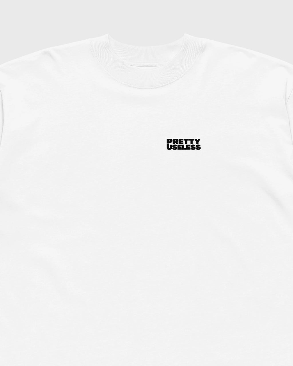 Detail des kleinen schwarzen PRETTY USELESS Logos auf der Vorderseite des weißen ANGEL T-Shirts.