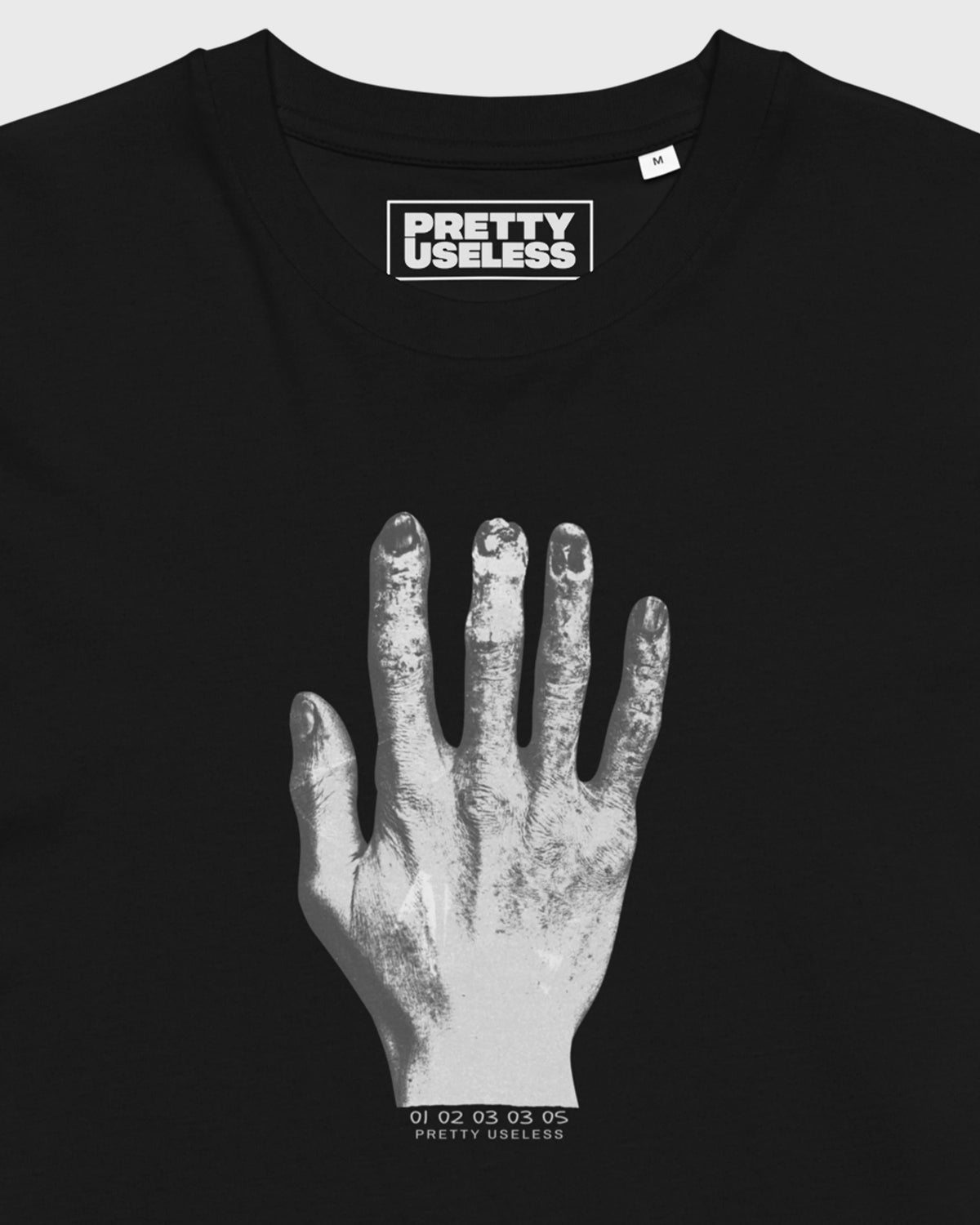 Detailansicht des hellen Handprints und PRETTY USELESS Nackenprints auf schwarzem T-Shirt.