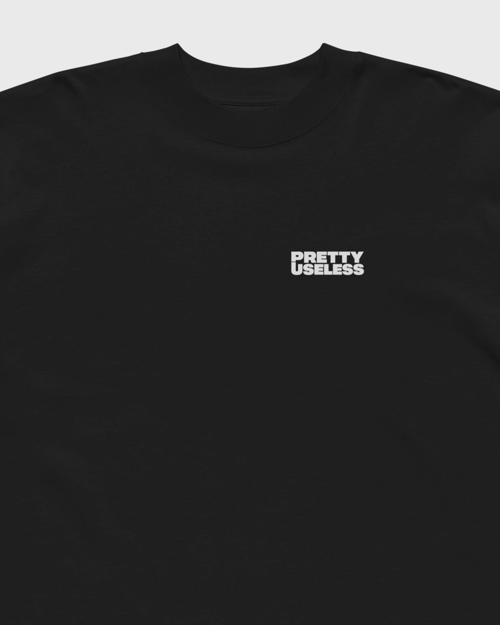 Detailansicht des kleinen PRETTY USELESS Logo-Prints auf der Brust eines schwarzen Oversized T-Shirts.