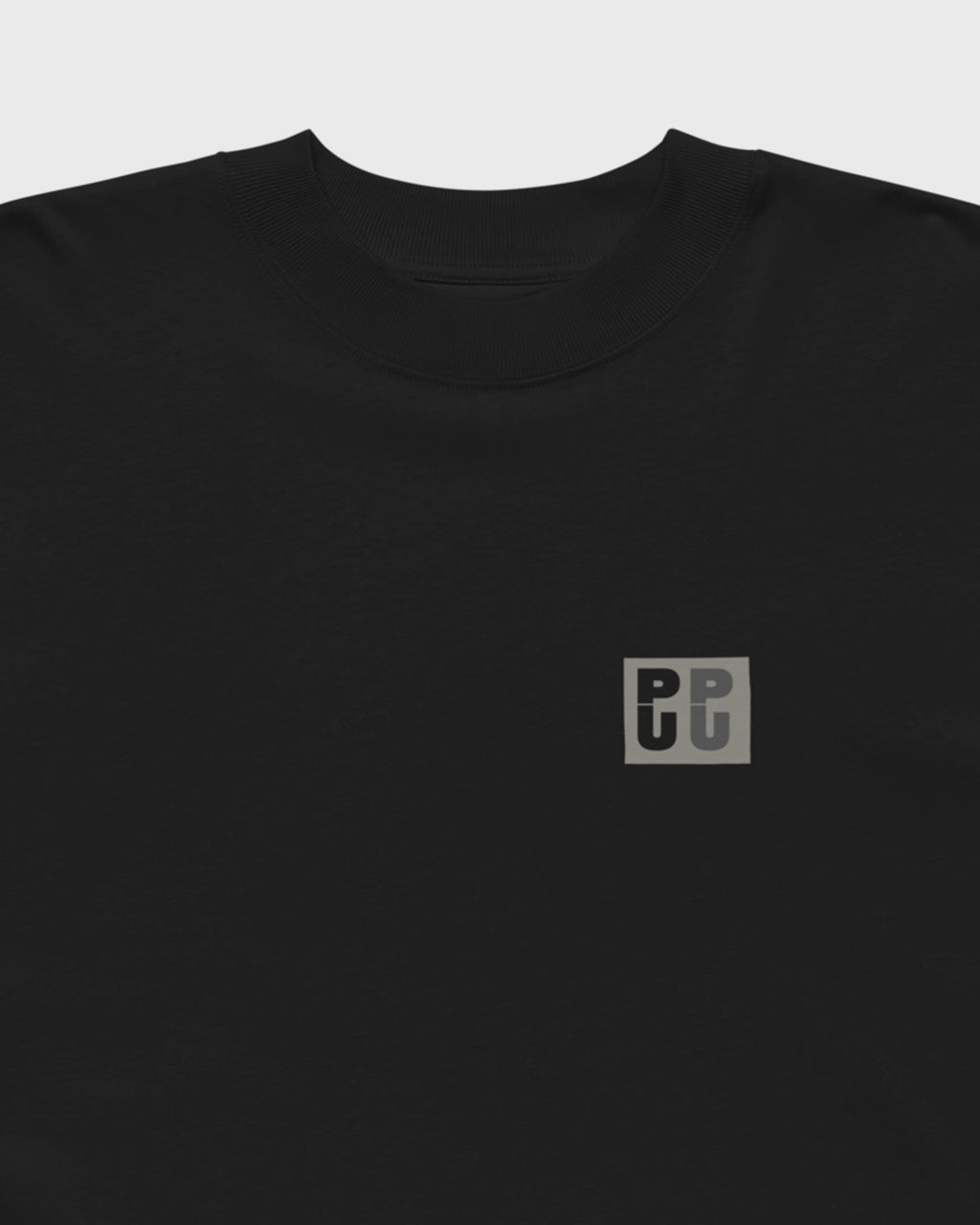 Detailansicht des kleinen grauen PU Logos auf der Brust eines schwarzen PRETTY USELESS Oversized T-Shirts.