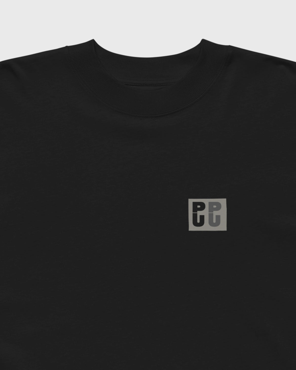 Detailansicht des kleinen grauen PU Logos auf der Brust eines schwarzen PRETTY USELESS Oversized T-Shirts.