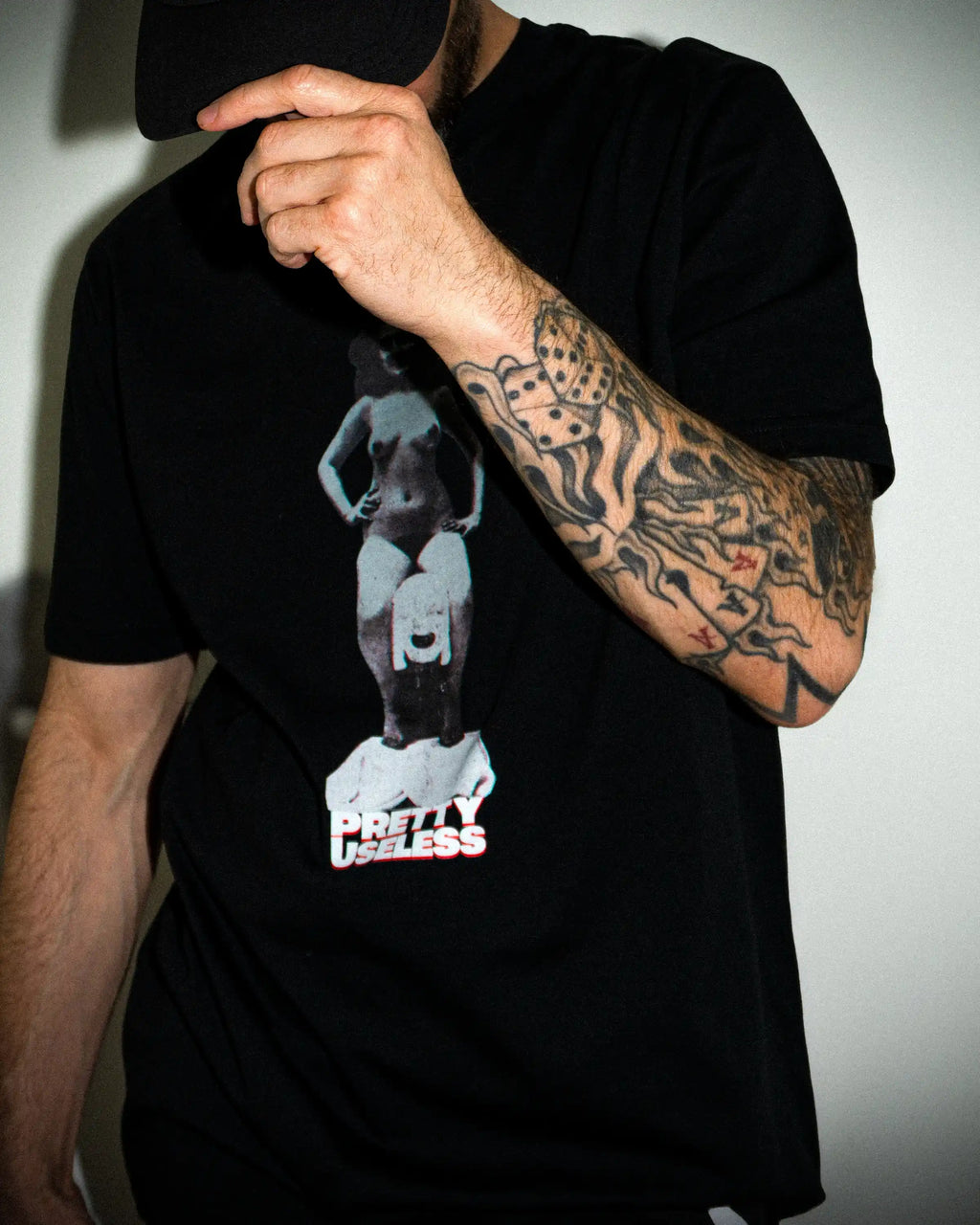 Model trägt ein schwarzes PRETTY USELESS T-Shirt mit surrealem Frauenmotiv auf der Vorderseite.