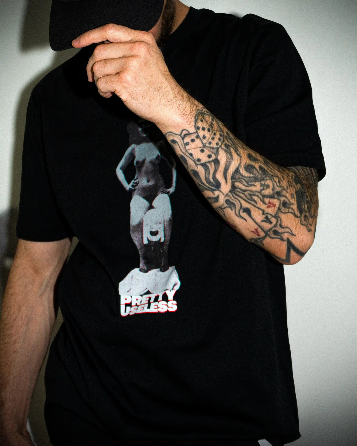 Model trägt ein schwarzes PRETTY USELESS T-Shirt mit surrealem Frauenmotiv auf der Vorderseite.