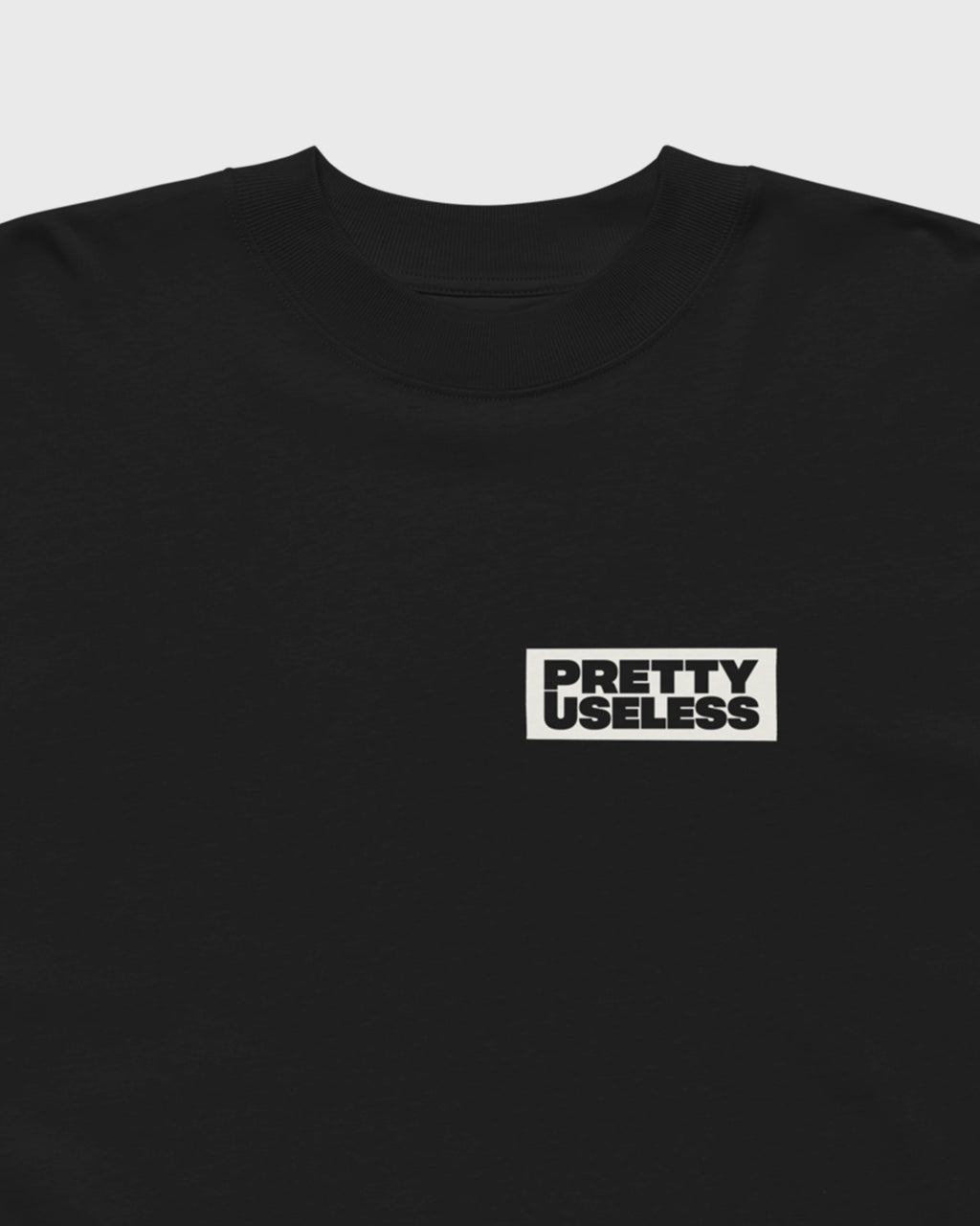 Detailansicht des kleinen PRETTY USELESS Logo-Prints auf der Vorderseite eines schwarzen Oversized T-Shirts.