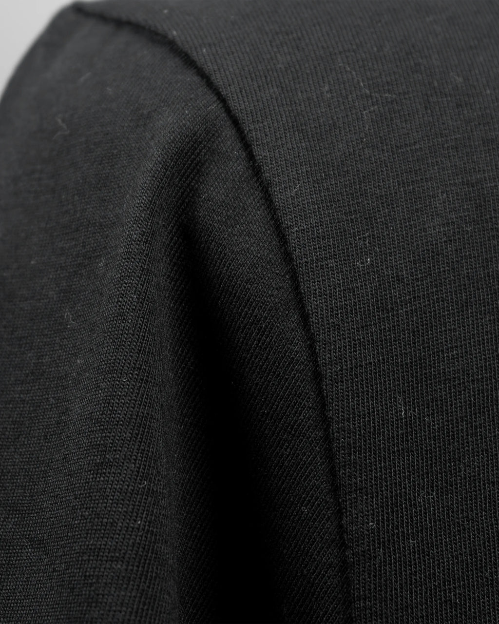 Detailaufnahme des schwarzen T-Shirt-Stoffs mit sichtbarer Baumwollstruktur und Naht.