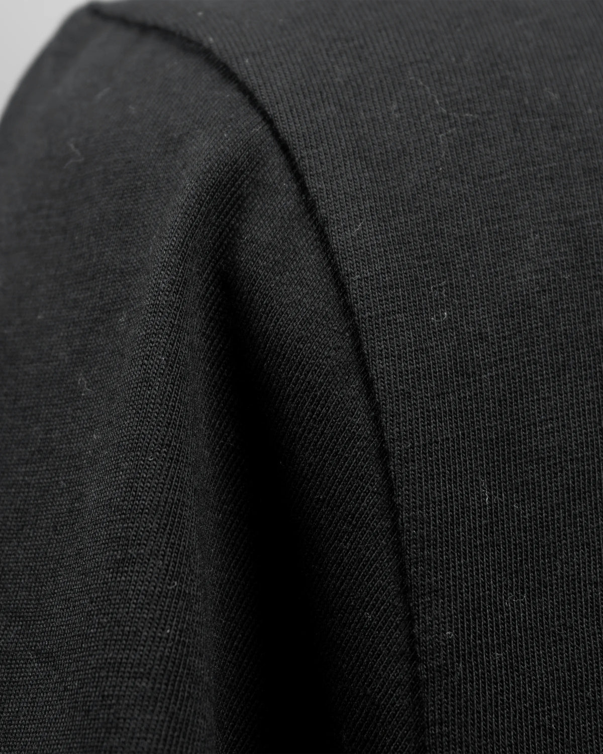 Detailaufnahme des schwarzen T-Shirt-Stoffs mit sichtbarer Baumwollstruktur und Naht.